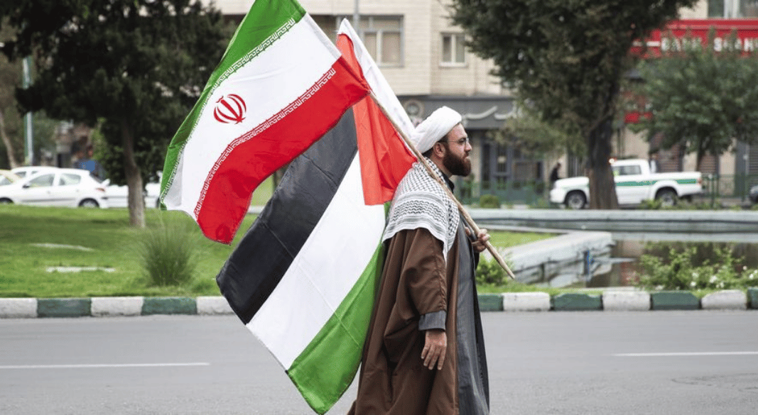 ইরানের তেহরানে শুক্রবারের নামাজের আগে ফিলিস্তিনিপন্থী সমাবেশে একজন মুসলিম ধর্মগুরু ফিলিস্তিনি ও ইরানি পতাকা ধরে আছেন